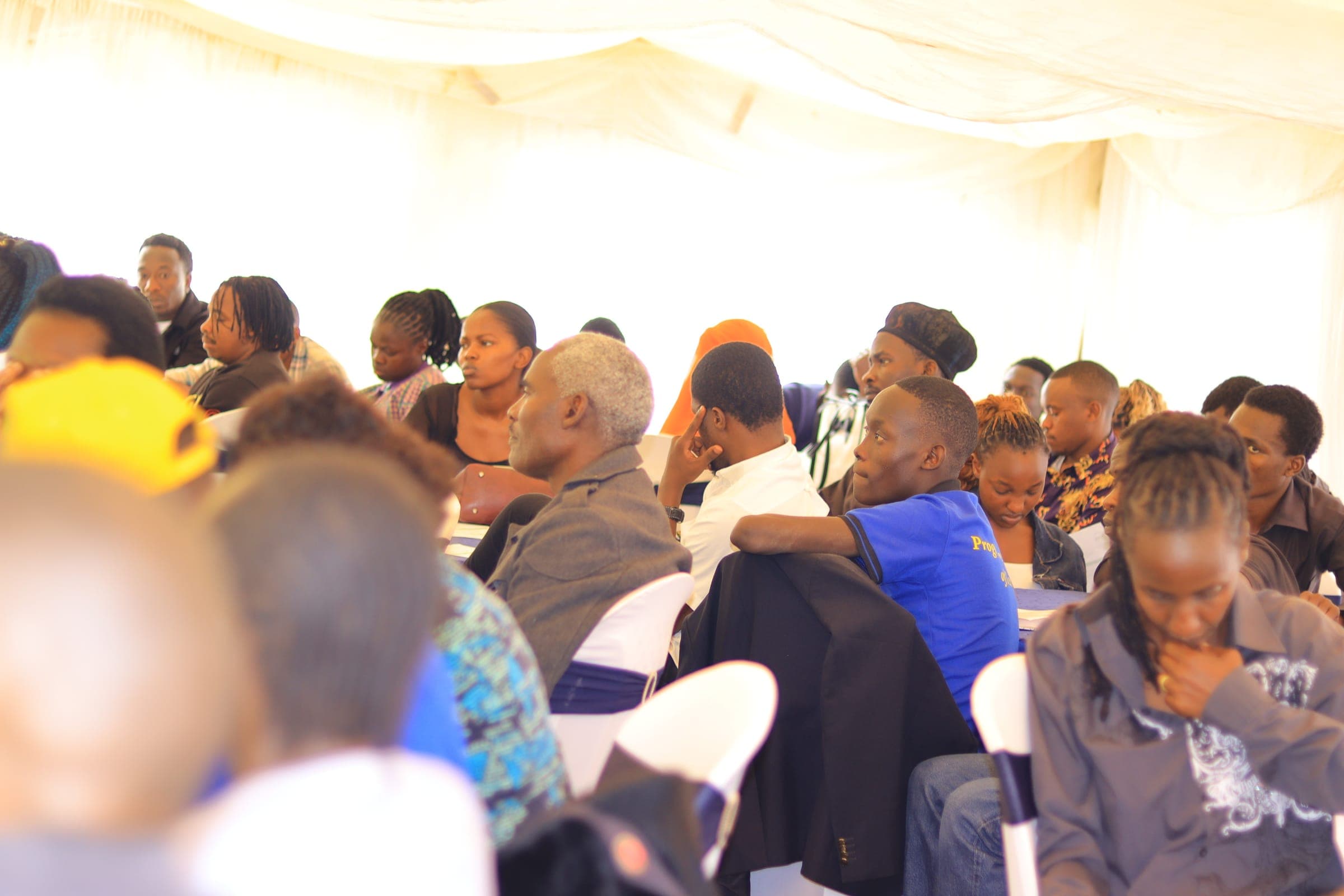 Party members seated at tables inside a white tent, listening to a session